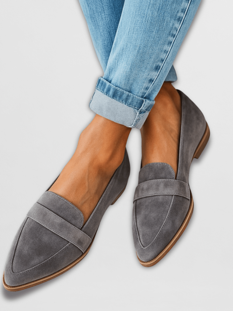 A woman wearing black suede loafers, styled with tailored trousers, walking on a city sidewalk, emphasizing everyday elegance.