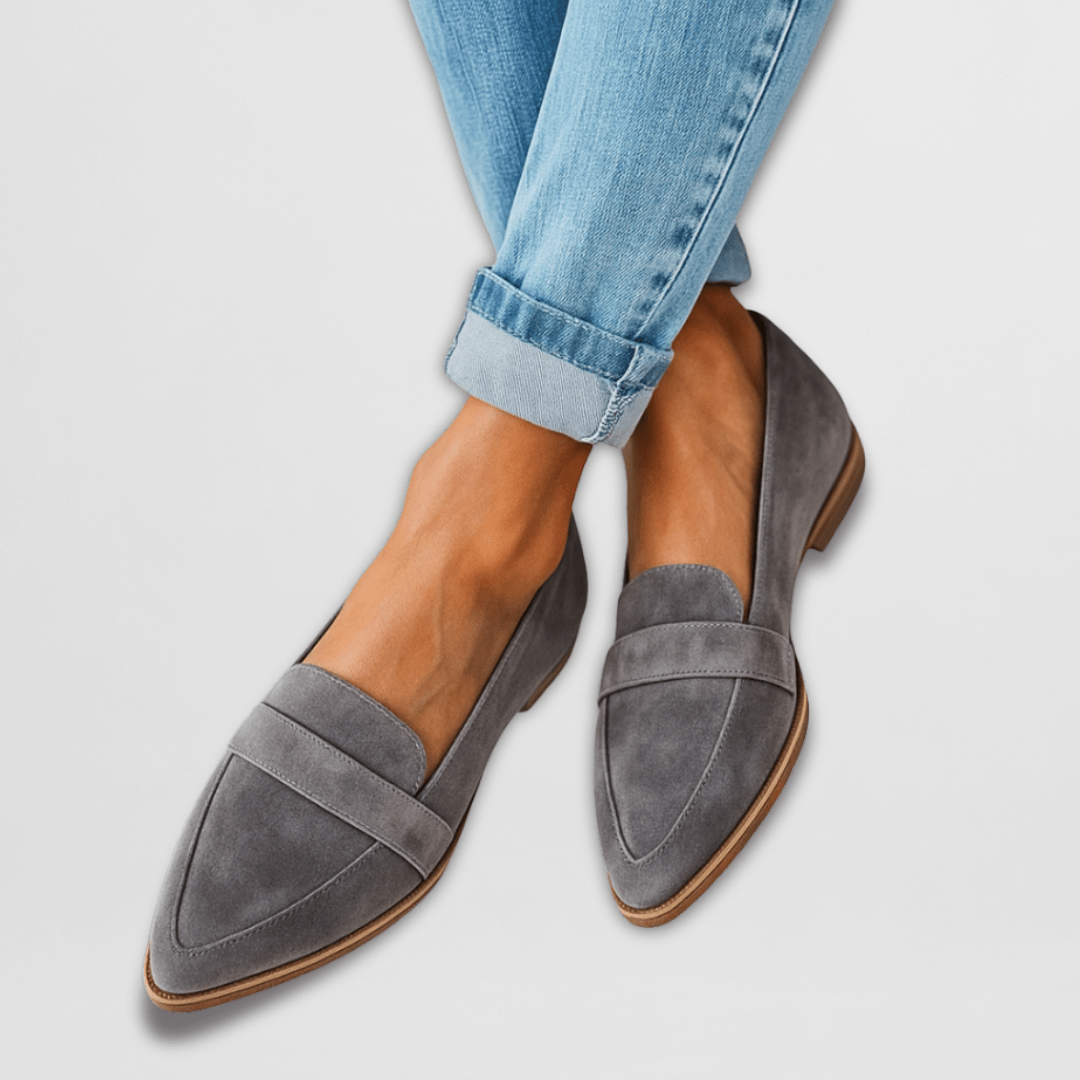 A woman wearing black suede loafers, styled with tailored trousers, walking on a city sidewalk, emphasizing everyday elegance.