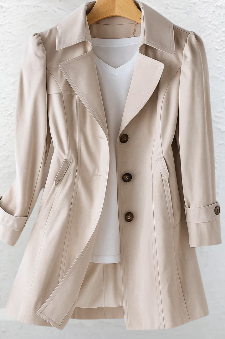 Close-up detail of the beige fabric and button closure of the Adeline trench coat, highlighting material quality.