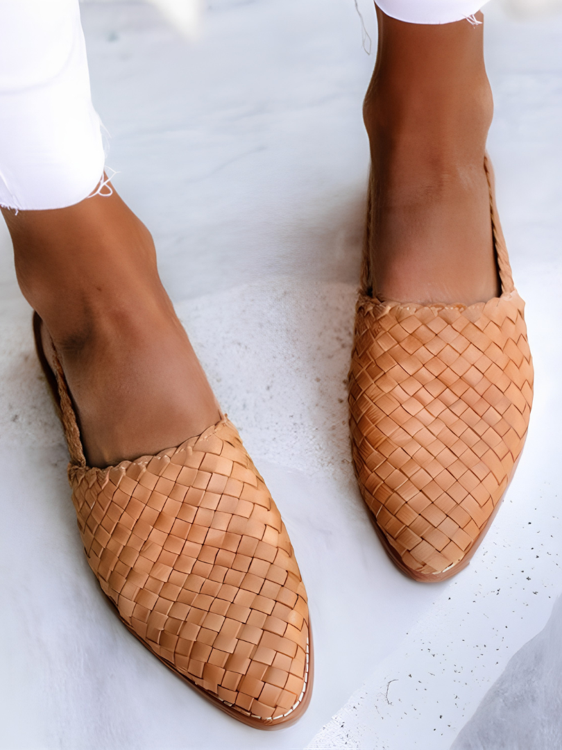 A woman wearing light brown handcrafted moccasins, walking on a paved path, demonstrating their comfort and style.