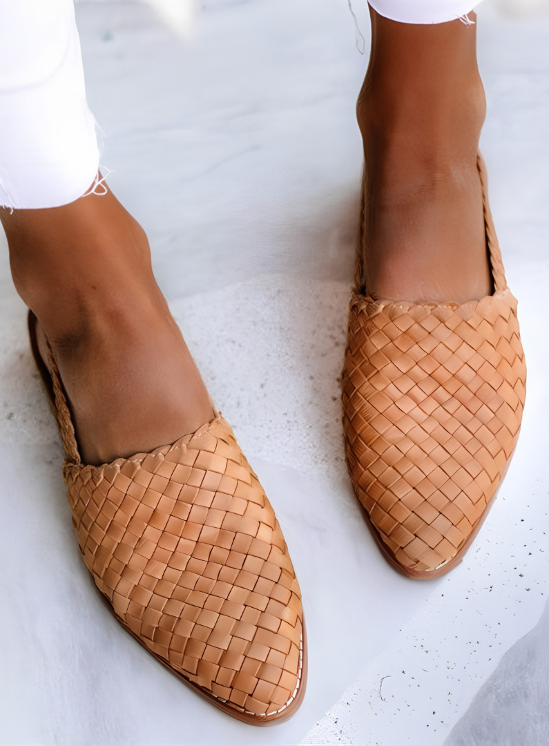 A woman wearing light brown handcrafted moccasins, walking on a paved path, demonstrating their comfort and style.