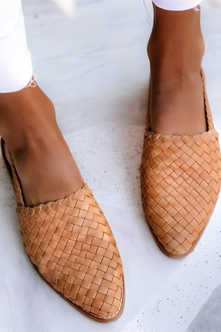 A woman wearing light brown handcrafted moccasins, walking on a paved path, demonstrating their comfort and style.