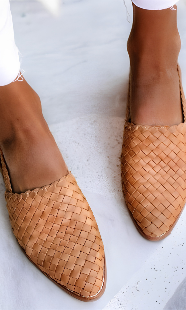 A woman wearing light brown handcrafted moccasins, walking on a paved path, demonstrating their comfort and style.