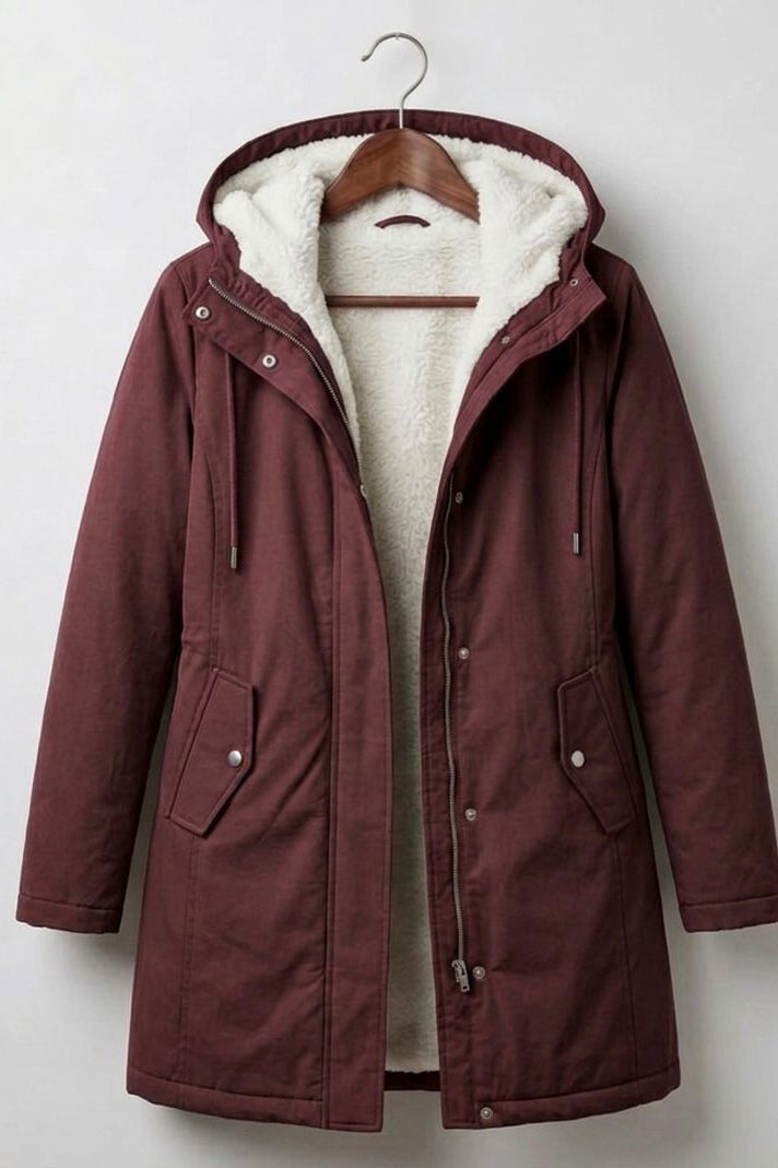A woman wearing the Elara waterproof parka in a natural outdoor setting, protected from light rain.