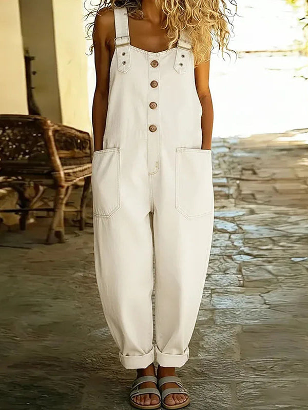 A model in white Hadley soft denim overalls, seated casually, illustrating the freedom of movement and relaxed styling.