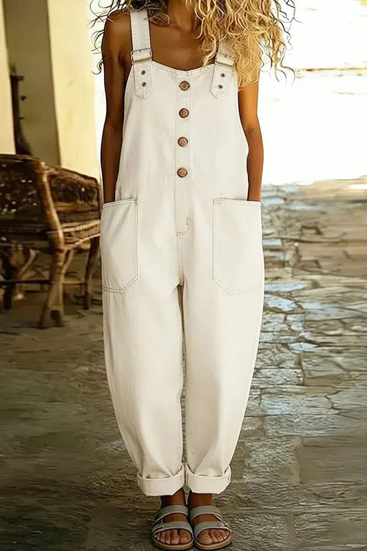 A model in white Hadley soft denim overalls, seated casually, illustrating the freedom of movement and relaxed styling.