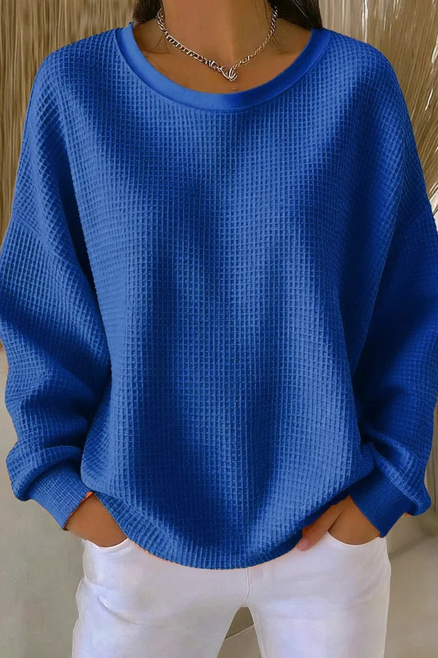Full-body shot of a woman wearing the Odette knit sweater in blue, paired with casual bottoms.