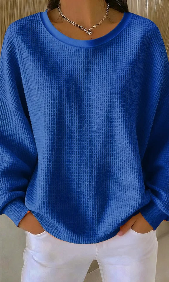 Full-body shot of a woman wearing the Odette knit sweater in blue, paired with casual bottoms.
