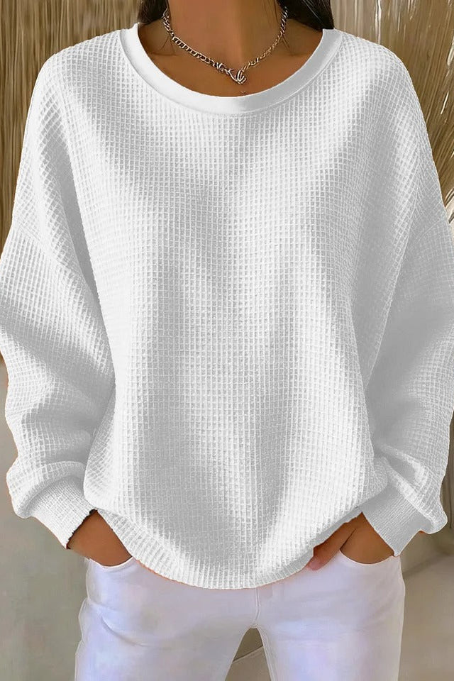 The Odette knit sweater in white, laid flat to display its classic round neckline and simple hem.