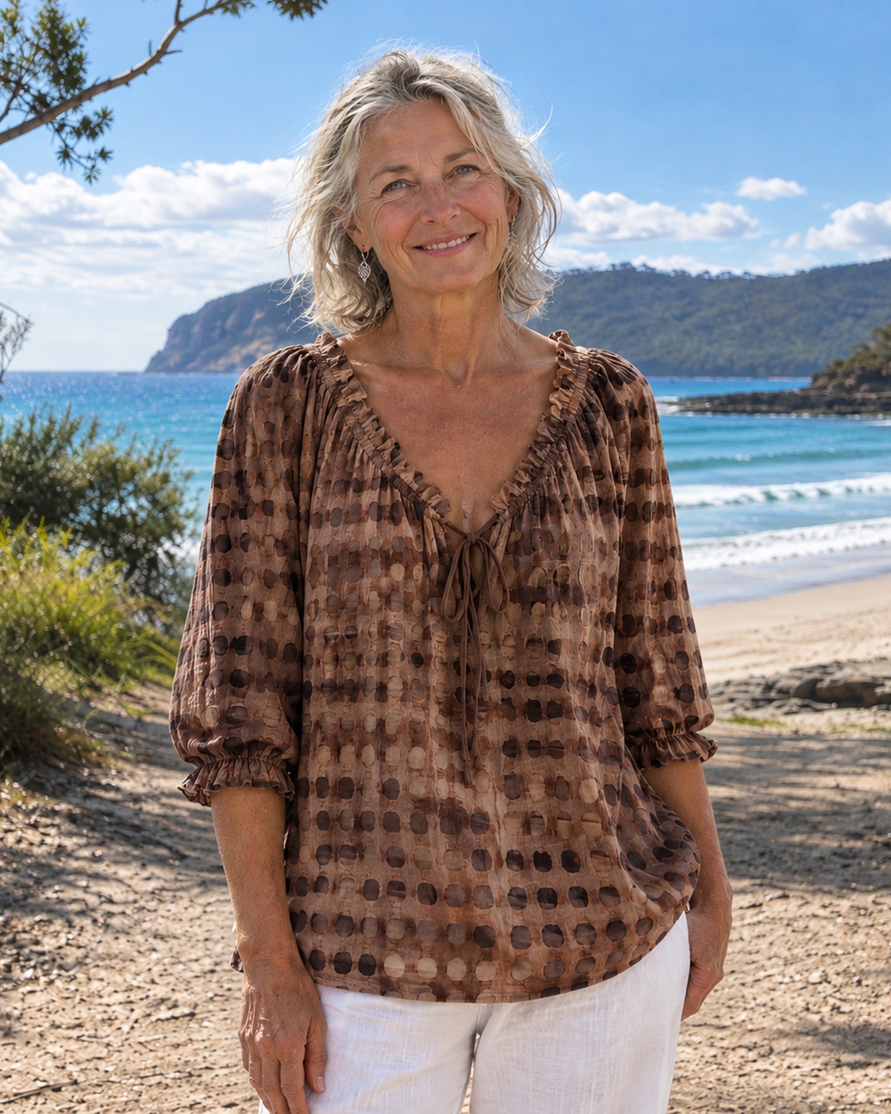 Close-up of the ruffled V-neckline on the brown Xylia blouse, detailing the tie closure.