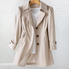 Close-up detail of the beige fabric and button closure of the Adeline trench coat, highlighting material quality.