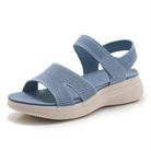 A woman wearing beige arch support walking sandals while strolling outdoors on a paved path, active lifestyle.