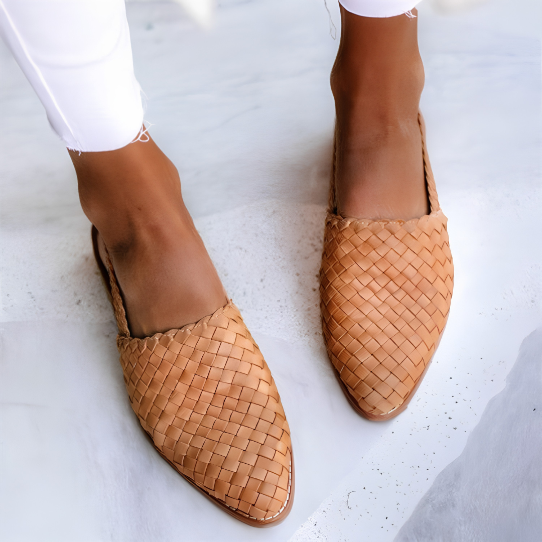A woman wearing light brown handcrafted moccasins, walking on a paved path, demonstrating their comfort and style.