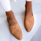 A woman wearing light brown handcrafted moccasins, walking on a paved path, demonstrating their comfort and style.