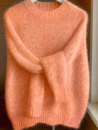 Lifestyle image of a woman enjoying a cup of coffee while wearing the white Elara cashmere-blend sweater, depicting comfort.