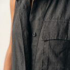 Close-up detail of the olive sleeveless jumpsuit's partial button placket and chest pocket.