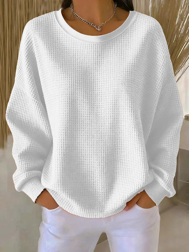 The Odette knit sweater in white, laid flat to display its classic round neckline and simple hem.