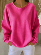 A model smiling while wearing the Odette knit sweater in fuchsia, showcasing comfort and confidence.