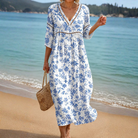 A woman confidently wearing the Thora floral beach midi dress, showcasing its flowing blue fabric and comfortable, relaxed fit in a sunny outdoor setting.